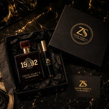 Two perfume bottles and a box with Zavya Scents' branding on a dark marble surface.