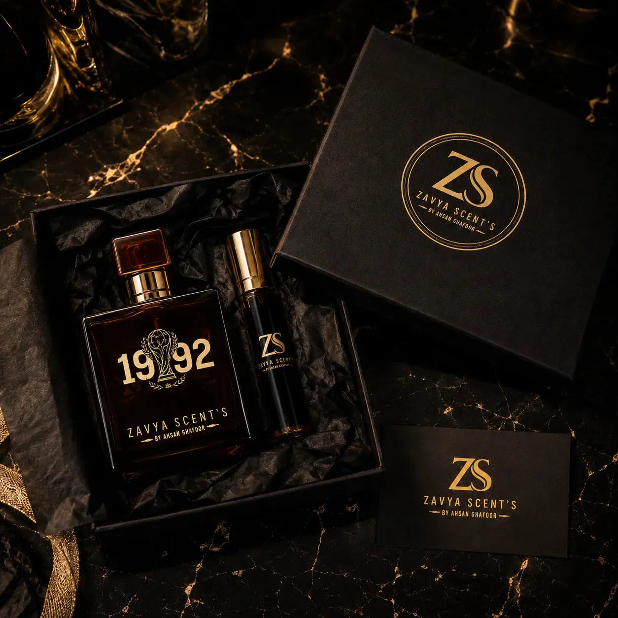 Two perfume bottles and a box with Zavya Scents' branding on a dark marble surface.